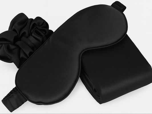 Black satin eye mask and hair tie on a white background