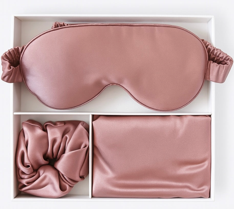 Pink silk eye mask, hair tie, and pouch in a white box on a white background